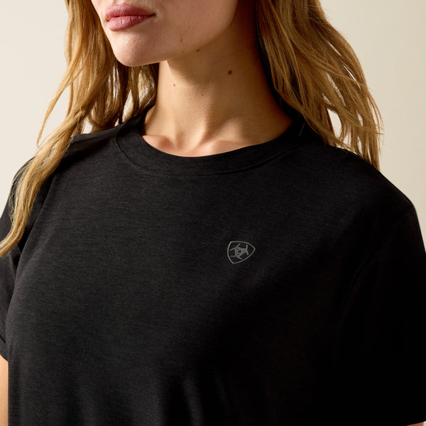 Person wearing a black t-shirt with a logo on a beige background