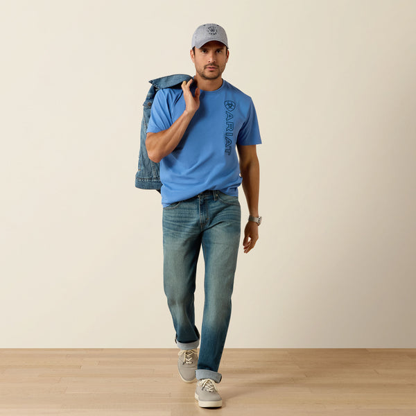 Man wearing a blue t-shirt and jeans, holding a denim jacket, on a plain background