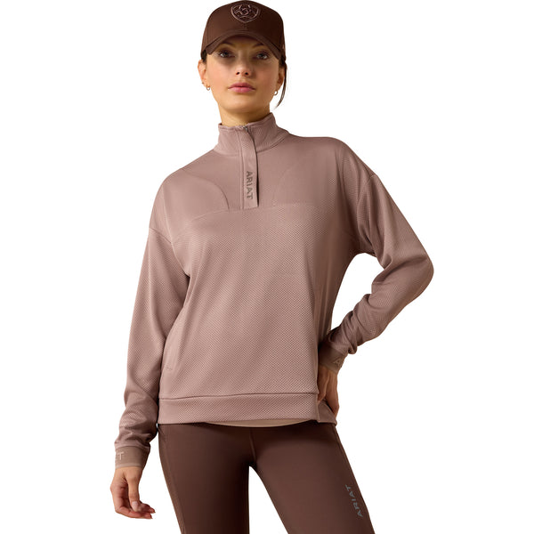 Woman wearing a brown quarter-zip pullover and cap on a white background
