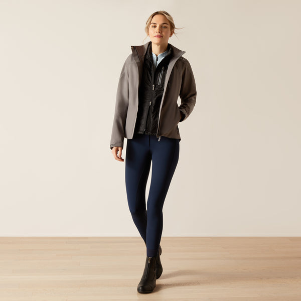 Woman wearing a layered outfit with a jacket, shirt, and pants on a plain background