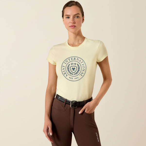 Woman wearing a cream t-shirt with a logo and brown pants on a beige background