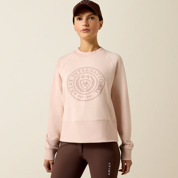 Person wearing a pink sweatshirt with a logo and brown pants on a beige background