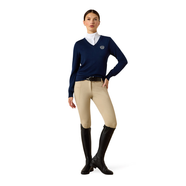 Woman wearing a navy sweater, beige riding pants, and black riding boots on a white background