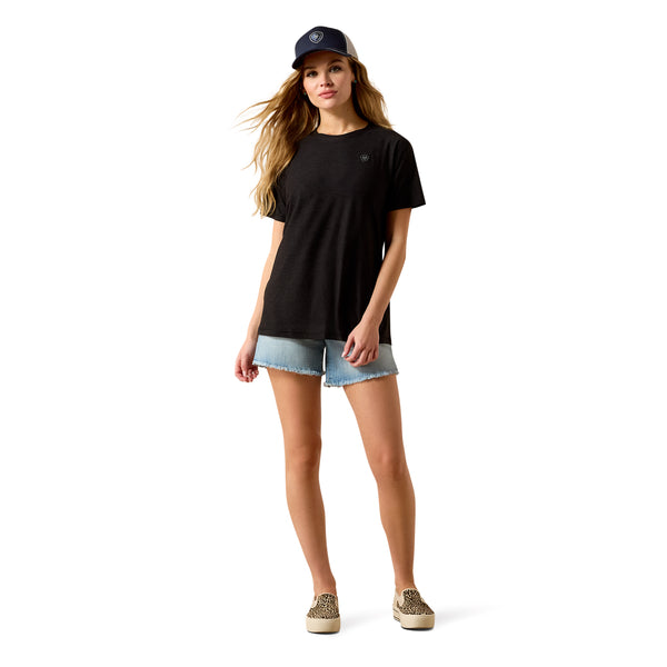 Woman wearing a black t-shirt, denim shorts, and a cap on a white background